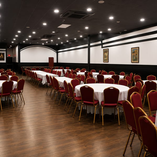 Spacious banquet hall with round tables, white tablecloths, and red chairs, ready for an event.
