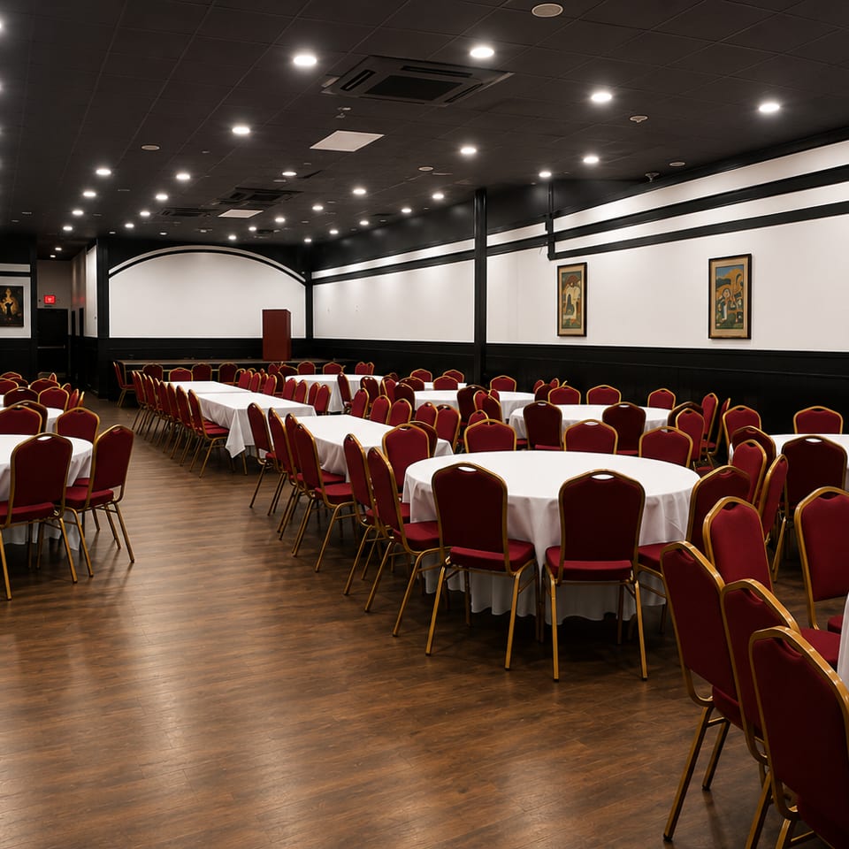 Spacious banquet hall with round tables, white tablecloths, and red chairs, ready for an event.
