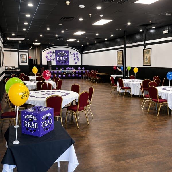 Spacious restaurant dining room set up for a graduation party with purple and yellow decorations.