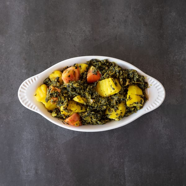 A white oval dish filled with saag aloo, a green spinach and potato curry with tomatoes.