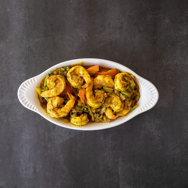 Curried shrimp with vegetables in a white oval dish on a dark gray surface.