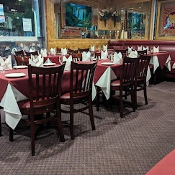 Restaurant dining room with red tablecloths, dark wooden chairs, and a TV on the wall.