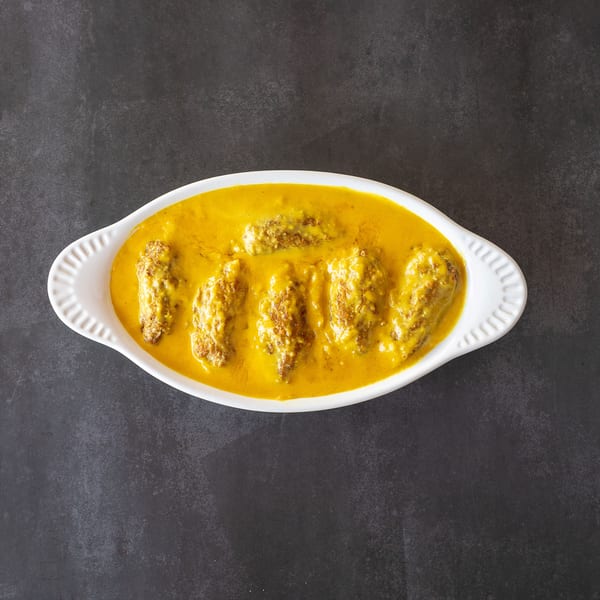 White oval dish filled with five pieces of kofta in a rich yellow curry sauce.