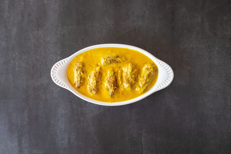 White oval dish filled with five pieces of kofta in a rich yellow curry sauce.