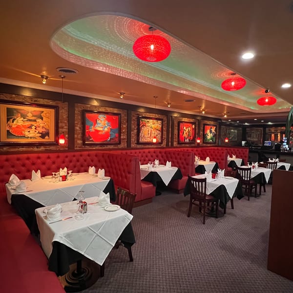 Restaurant interior with red booth seating, white-clothed tables, and colorful framed artwork on brick walls.