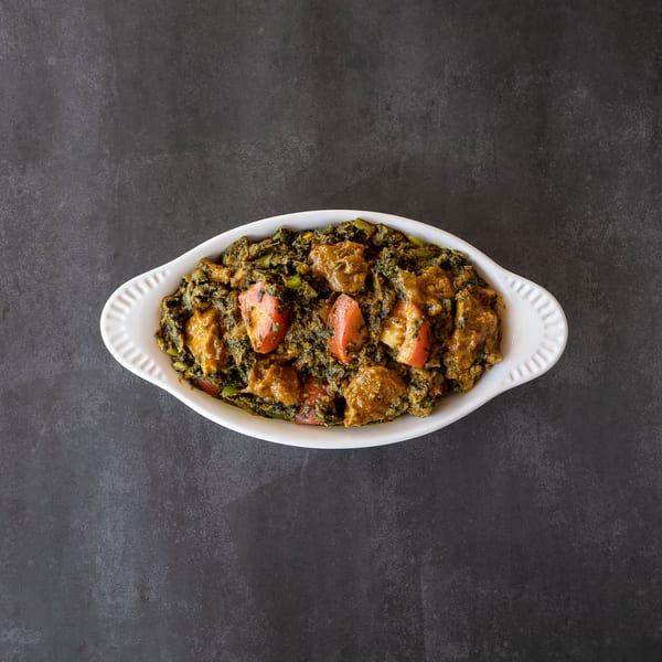 Overhead view of a white dish filled with a green curry, chicken, and tomato wedges.