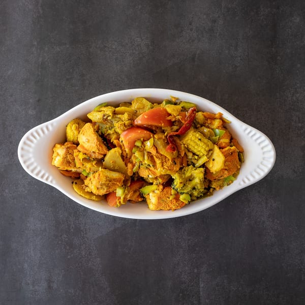 Colorful vegetable stir-fry with tofu, broccoli, tomatoes, and baby corn in a white dish.