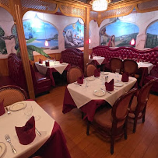 Empty restaurant dining room with red booths, white tablecloths, and wall murals of scenic landscapes.
